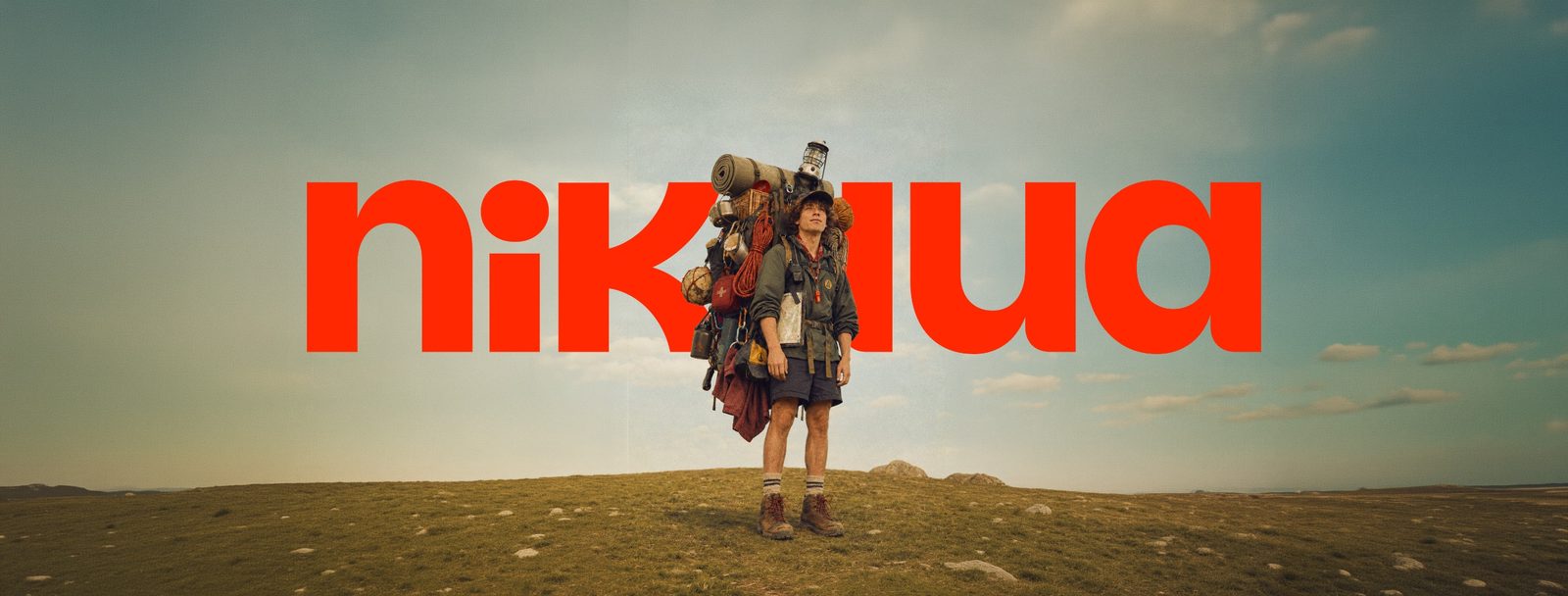 Monitor de campamento con la mochila cargada, de pie en la campa, sobre el logotipo de Nikaua